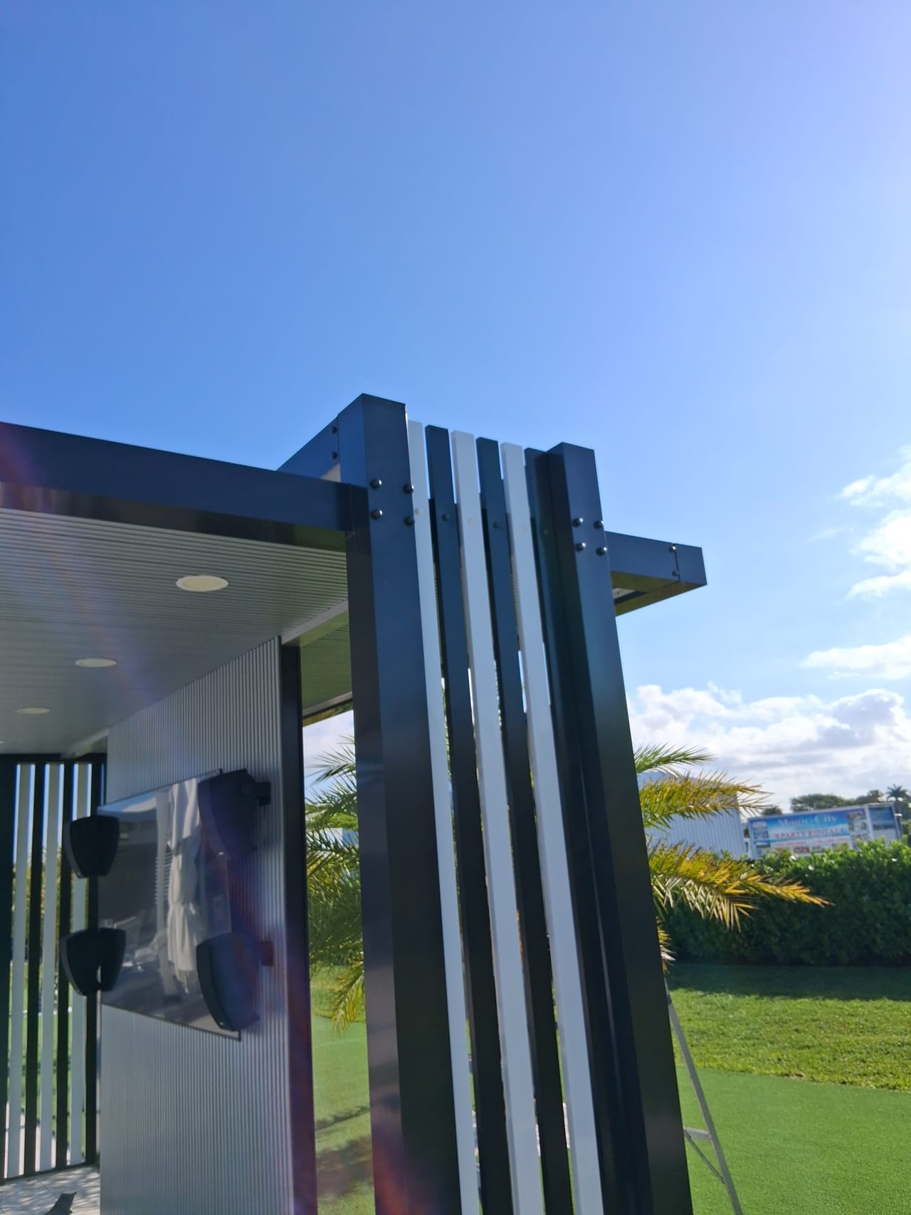 Close view of the bolted aluminum post and beam connection on a modern pergola, with alternating dark and light vertical slats
