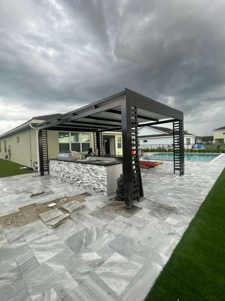 Dark open-rafter pergola with louvered end panels over a stacked-stone outdoor kitchen bar next to a backyard pool